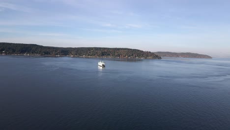 Fall-colors-dot-the-shoreline-as-a-vessel-ferry-crosses-calm-blue-waters,-aerial