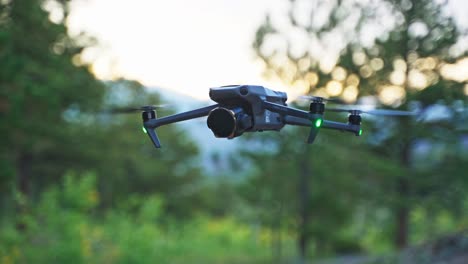 drone hovering in front of forested landscape during golden hour, with soft sunlight highlighting the trees in the background