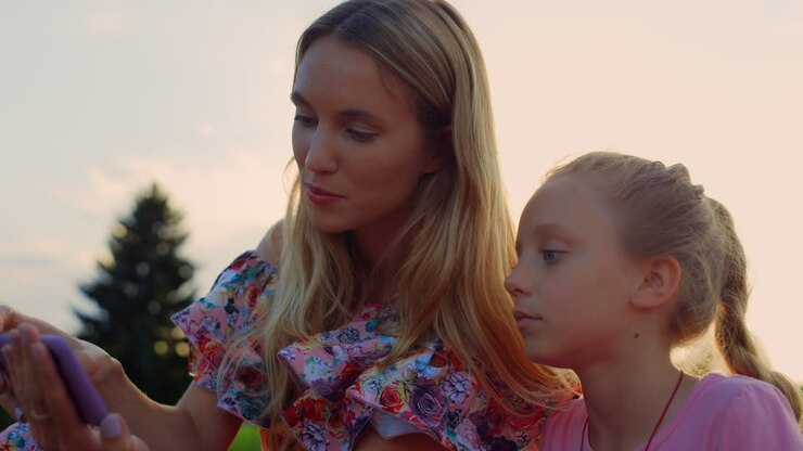 Mutter und Tochter schauen im Freien auf ein Handy. Familie hört Musik.