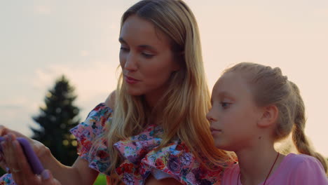 madre e hija mirando el teléfono móvil al aire libre. familia escuchando música.