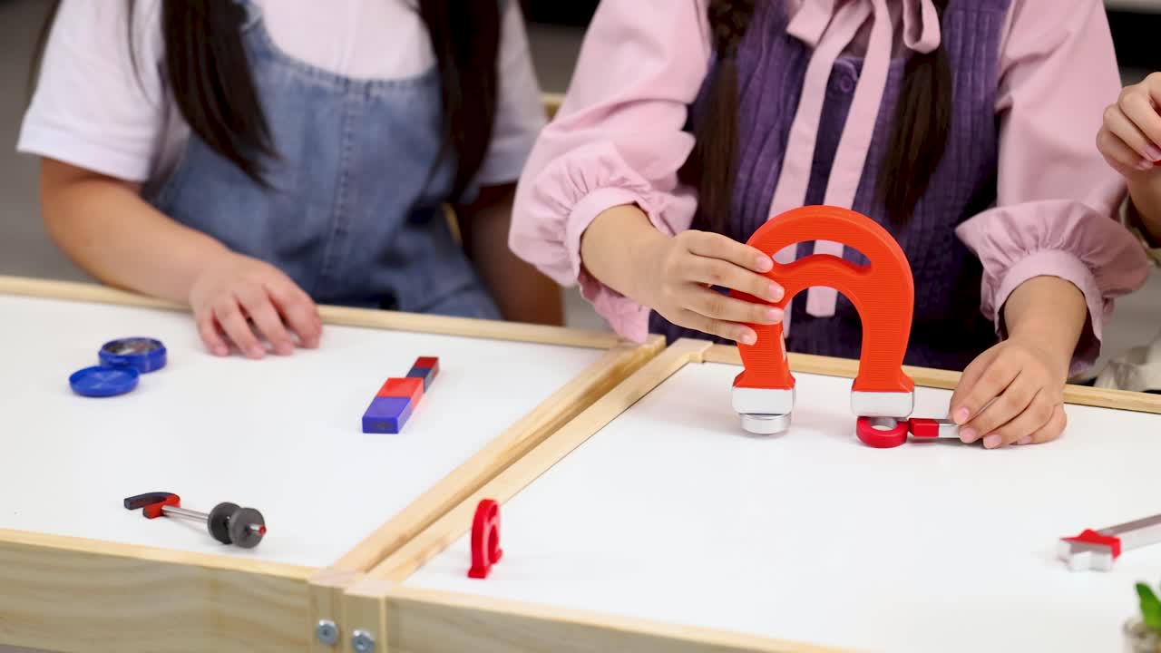 Close-up of students' hands conducting a physics experiment using magnets on a white table