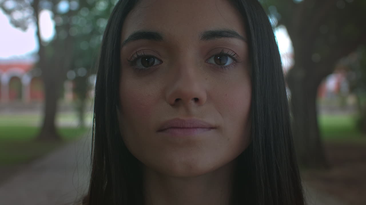 High-quality 4K shot of a young brunette in natural light, slowly opening her eyes in a park setting. She has a peaceful, daydreaming expression. Ideal for nature, mindfulness,