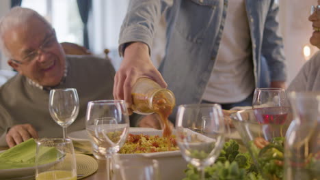 hombre adulto irreconocible vertiendo salsa en el plato y el abuelo viéndolo durante la cena familiar en casa