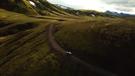 aerial landscape view over a four wheel drive car traveling on a mountain dirt road through icelandic highlands