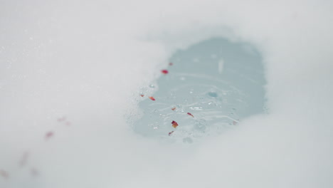 salt crystals and petals fall down into foamy water closeup. aromatic organic cosmetic product and dry plants for spa care in bathroom. bodycare routine