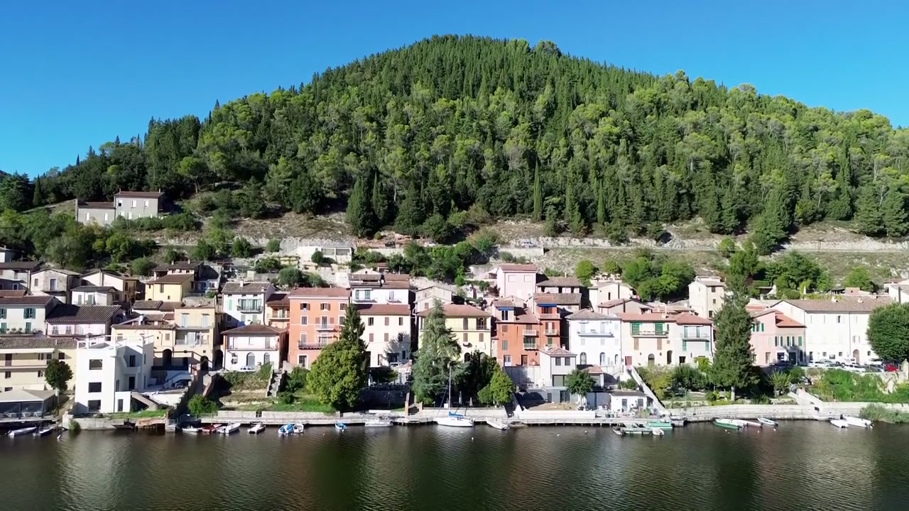 Veduta aerea con drone della città collinare di Piediluco in Umbria, Italia, che si affaccia sul calmo lago di Piediluco ed è circondata da rigogliose montagne verdi sotto cieli azzurri
