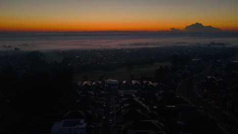 Drohnenaufnahme-Von-Wohngebieten-In-Ländlicher-Umgebung-Mit-Berghintergrund-Und-Orangefarbenem-Himmel