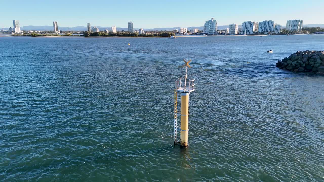 Drone footage captures a buoy and expansive waterway with the Gold Coast skyline in the background under clear skies