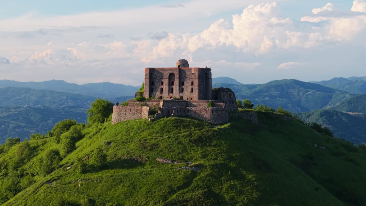 Ancient Italian fort perched atop a hill, surrounded by nature and distant mountains