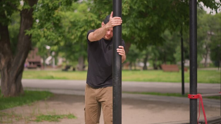 Persona appoggiata a un sostegno verticale dopo l'allenamento, uomo che si appoggia al palo di un parco dopo un'intensa sessione di training, individuo appoggiato a un palo verticale nel parco per riprendersi da un esercizio faticoso