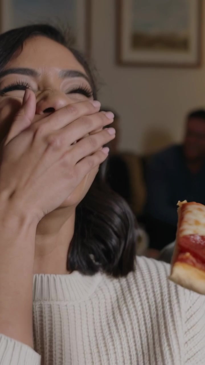 Vídeo vertical: Contendo o riso, mulher de suéter canelado segurando fatia de pepperoni em casa depois de uma piada