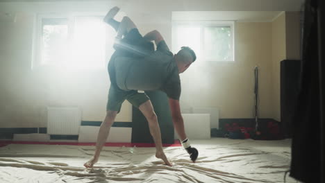 athlete throws down partner at sparring in sports club. young fighter attacks enemy exercising in foggy gym slow motion. hand to hand combat training