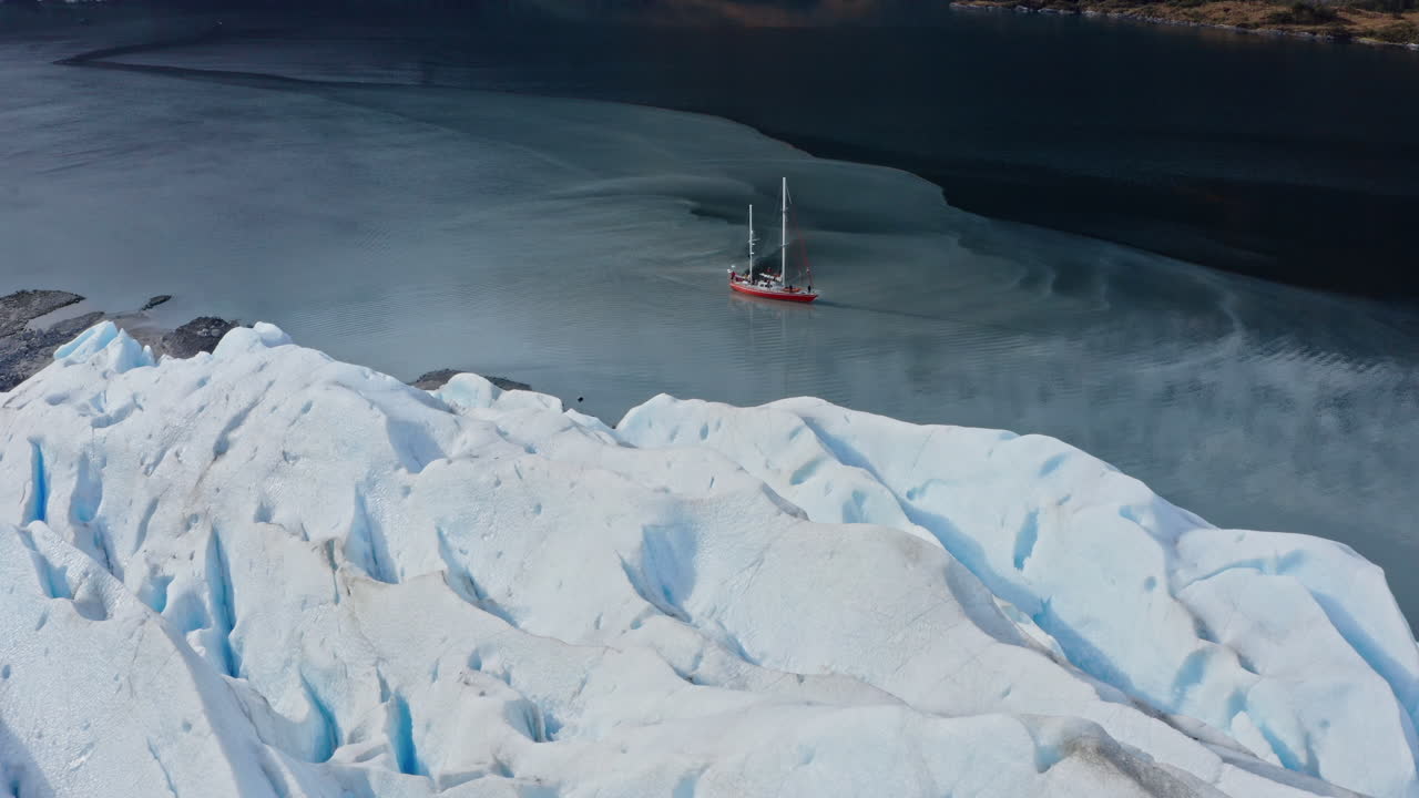 Glacial ice wall towers above Beagle Channel with cold water below and deep shadows above with sailboat in water