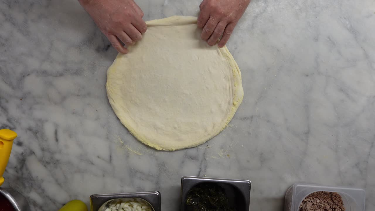 A chef prepares pizza dough to be topped, top-down shot