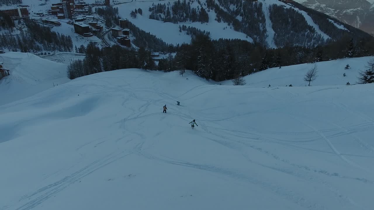 Veduta aerea con drone che segue un gruppo di snowboarder che scendono fuori pista. Ora del tramonto.