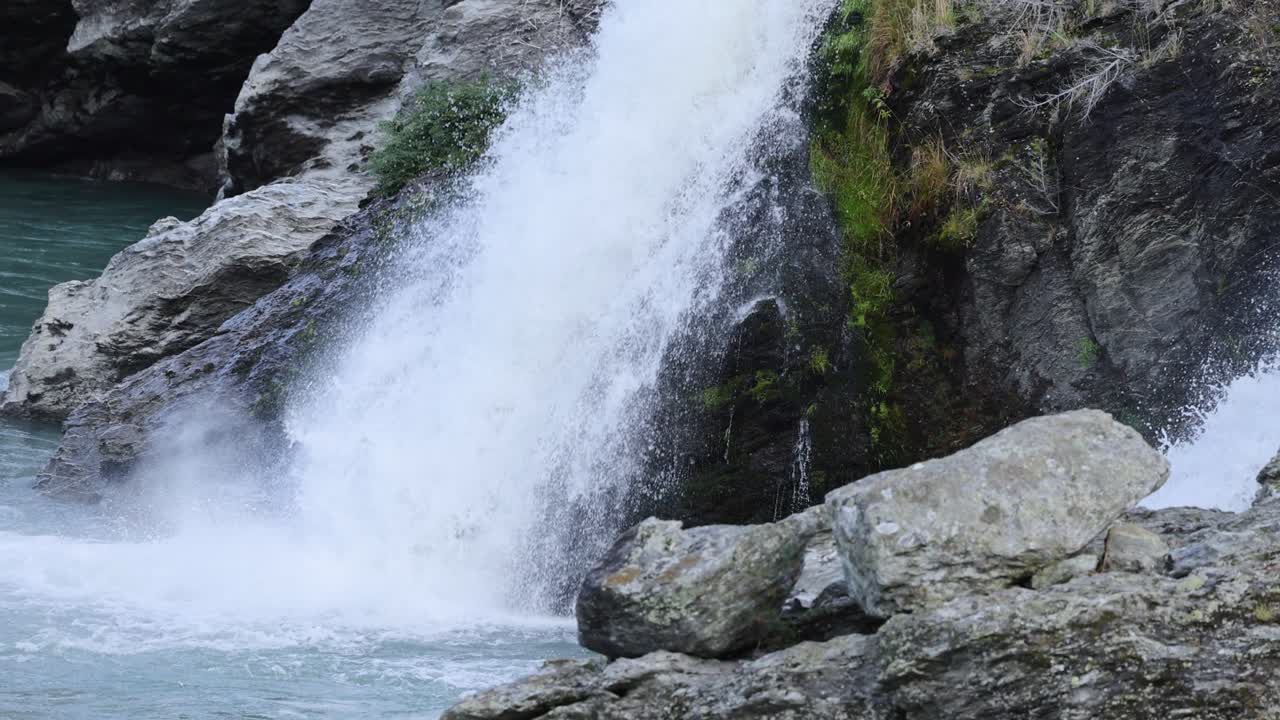 A powerful waterfall flows over rugged rocks in Queenstown, New Zealand, captured with dynamic movement and natural lighting