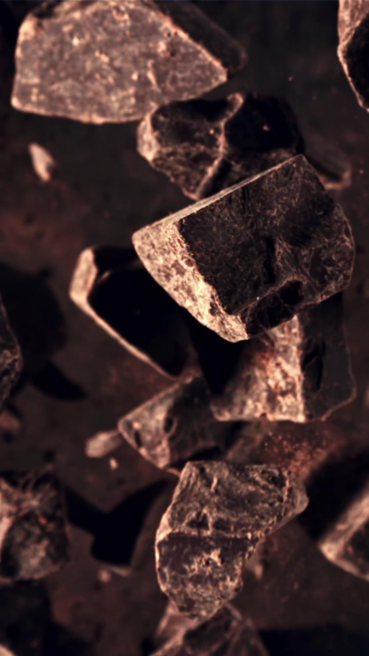 Trozos de chocolate negro cayendo en cámara lenta con polvo de cacao