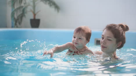 cute blonde toddler in protective glasses is diving under the water together with his mother in the swimming pool trying to take out his toy. his mother is teaching him how to swim. an underwater shot.