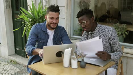 men working with laptop and papers in cafe