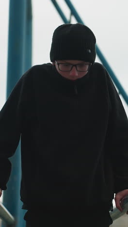 close-up of a young boy finishing a workout on a metal bar, dressed in a black outfit and glasses, after dropping from the bar, he walks away