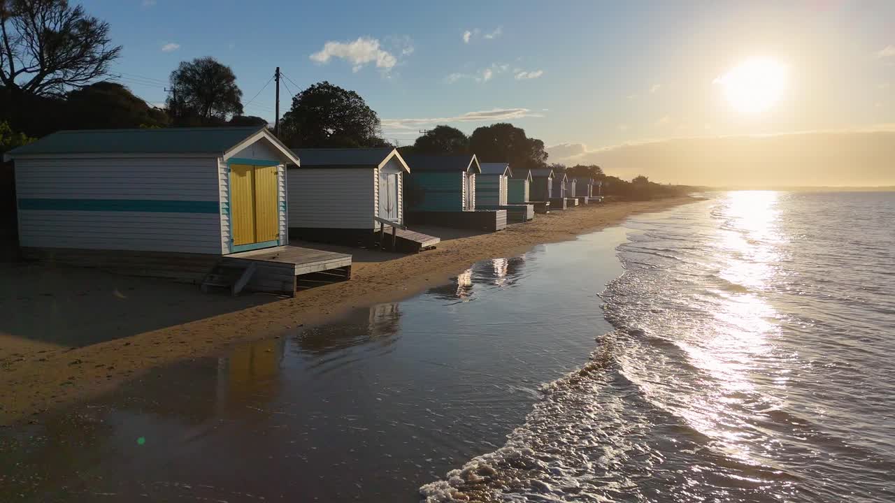 Low-angle tracking shot of bathing boxes, gentle waves, golden sunset light, tranquil beach atmosphere