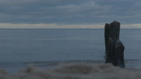 Wooden-posts-of-the-breakwater-close-to-the-shore,-wide-horizon-overlooking-the-sea