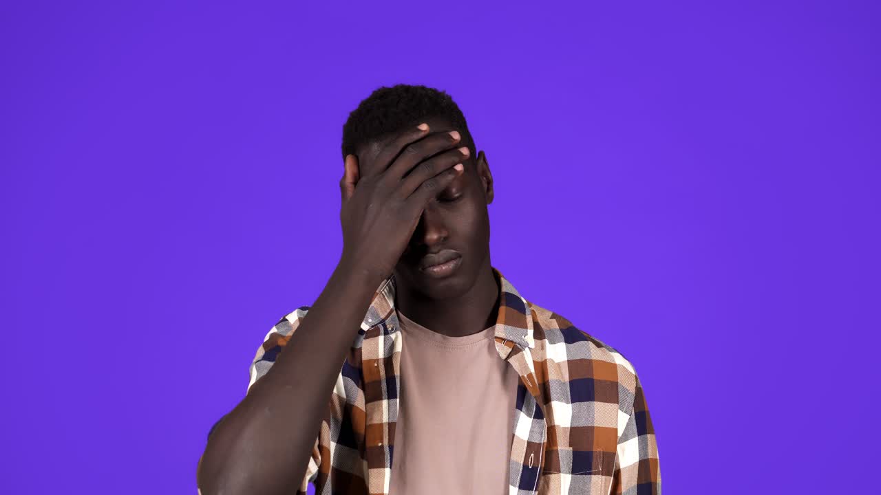 Portrait of dark-skinned young man rolling his eyes up isolated on blue background. Selfish man in plaid shirt tired