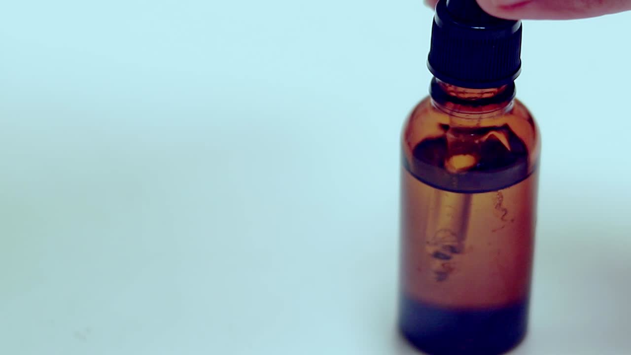 A brown glass bottle dropper containing natural organic herbal oil set against a soft blue background, creating a simple and minimalistic feel