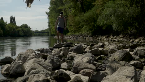 man stepping across rocks next to a river on a nature hike in slow motion