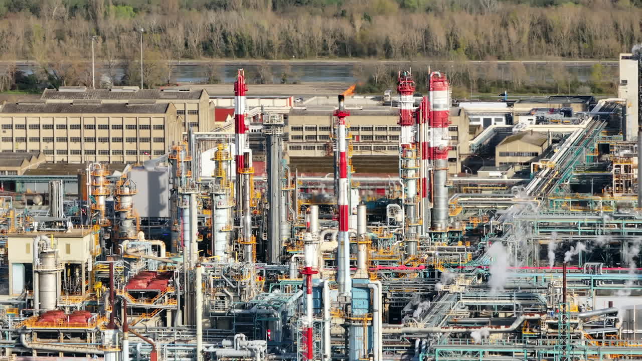 Busy industrial complex with active flares, detailed close-up of piping and machinery, daytime