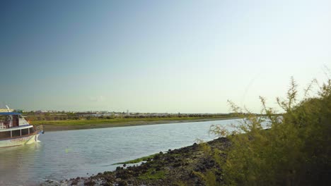 Morning-river-shore-with-ferryboat-passing-by-at-Tavira-Portugal