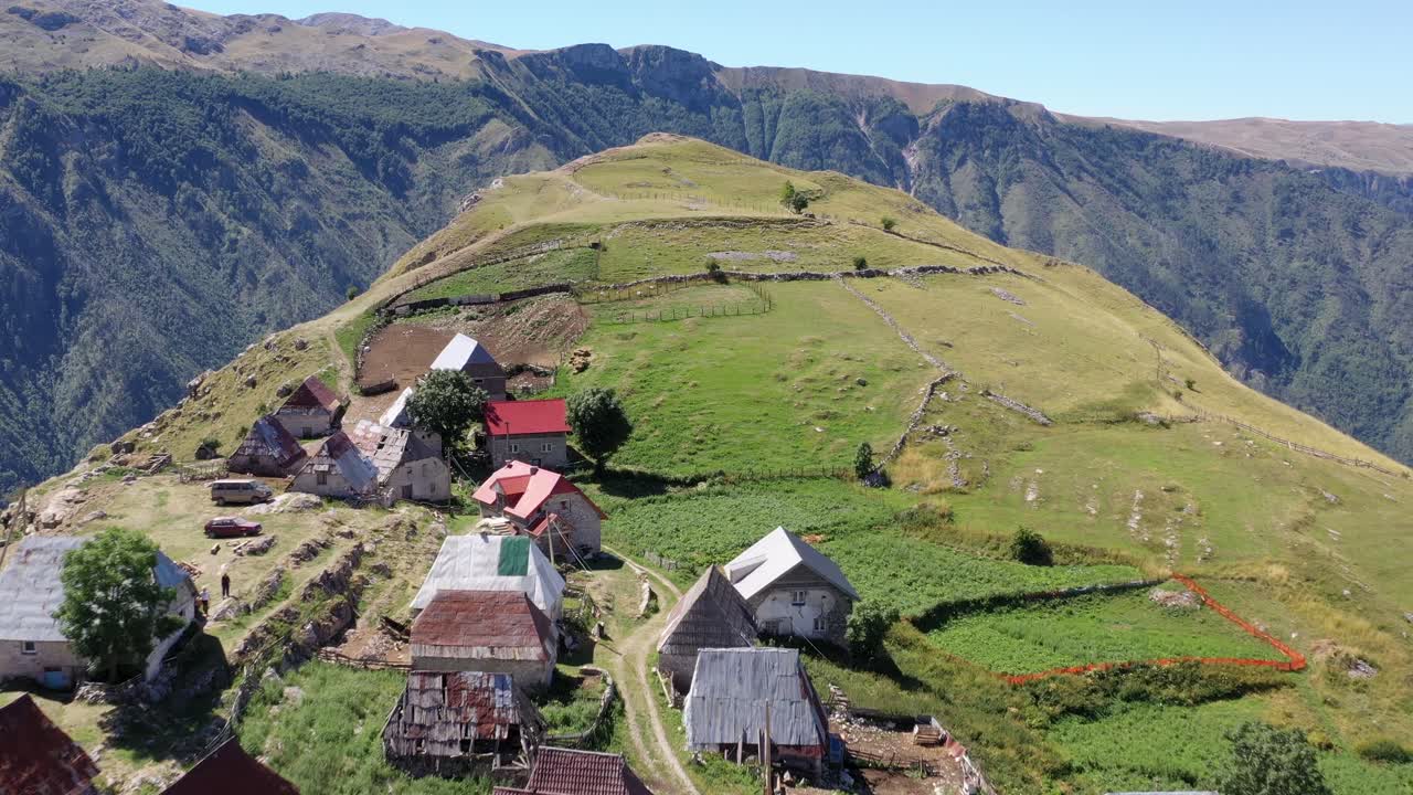 Small old farming village with adjacent fields on the slope of an enormous cliff in a mountain landscape. Drone shot