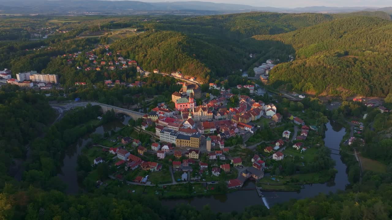 Sonnenuntergang über dem Dorf Loket und dem Fluss Eger inmitten von Bergen, Karlsbad