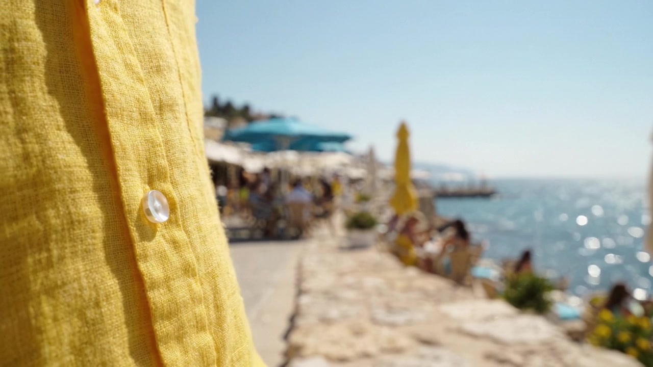 Uma Camisa Amarela Brilhante Capturada na Orla, Destacando o Deslumbrante Ambiente de Praia e a Vibrante Atmosfera Costeira com Visitantes Relaxados ao Fundo.
