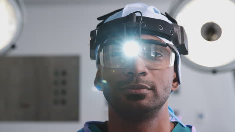 portrait of male surgeon with protective glasses and head light in hospital operating theater