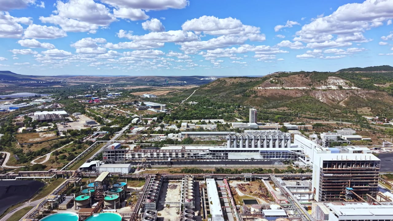 Industrial landscape with buildings, machinery, and hills in the background on a bright day