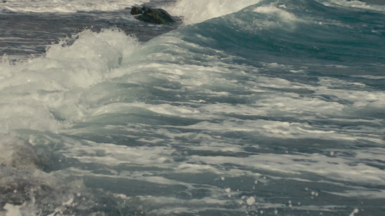 Close-up slow motion capture of an ocean wave breaking near shore, highlighting foam texture and sea motion in natural light