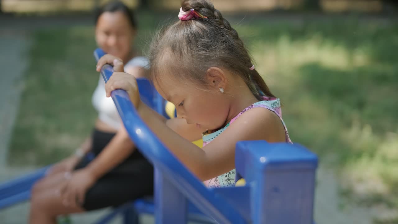 Mãe grávida e filha se exercitando em uma academia ao ar livre.