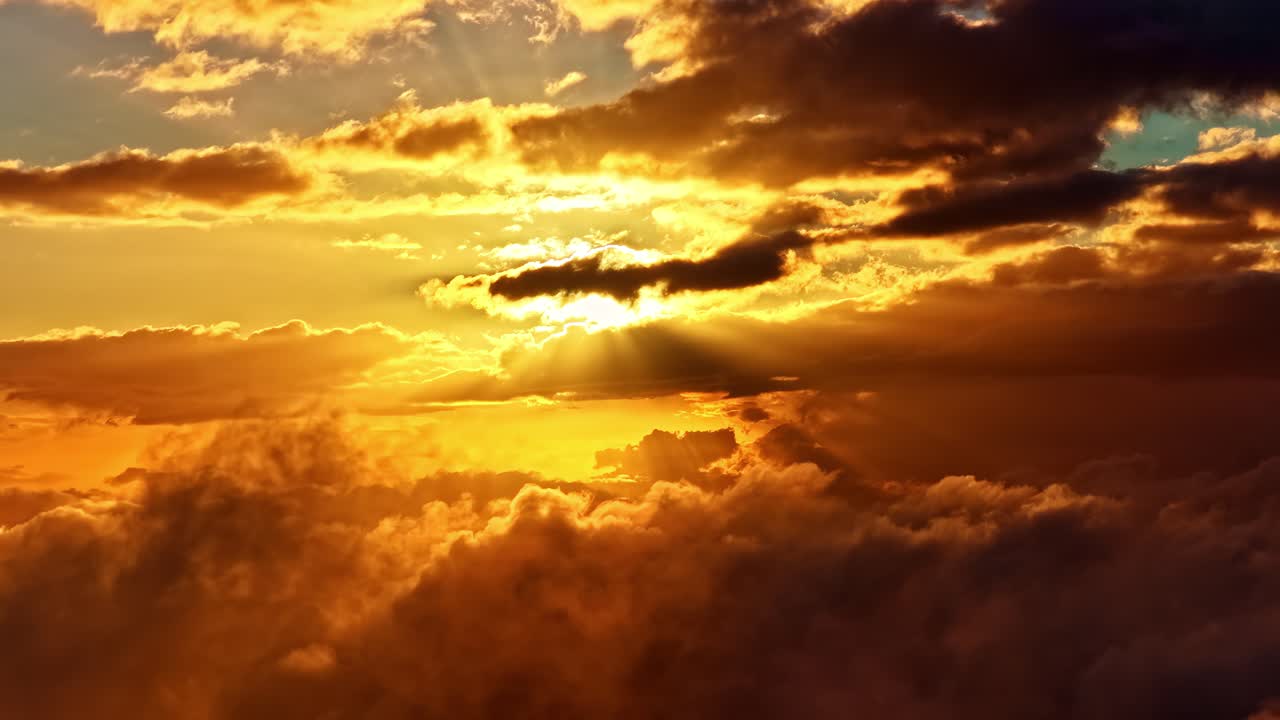 Sunset clouds stretching across golden sky above layered silhouetted hills, aerial heavenly rays pullback