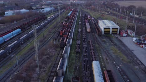 sunrise aerial view of long railroad tracks with heavy diesel locomotive carriages and cargo container yard forward tilt down