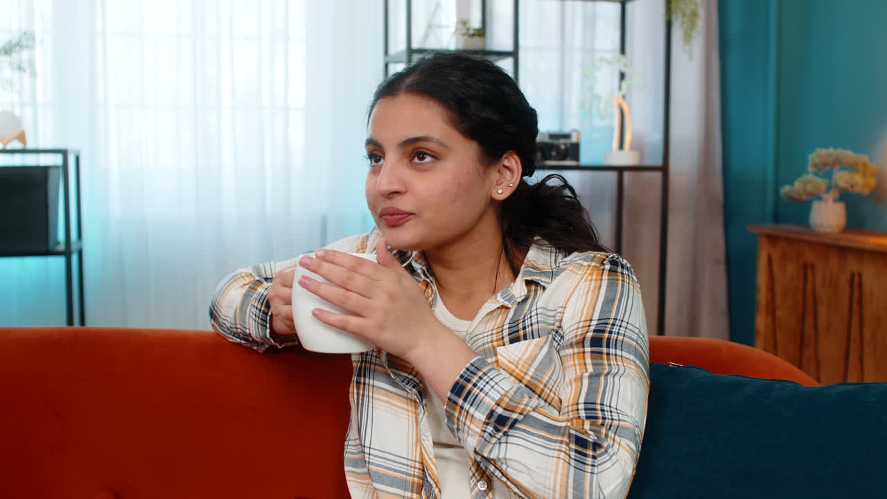 Indian woman drinking coffee looking thoughtfully out window solitude cozy morning home atmosphere