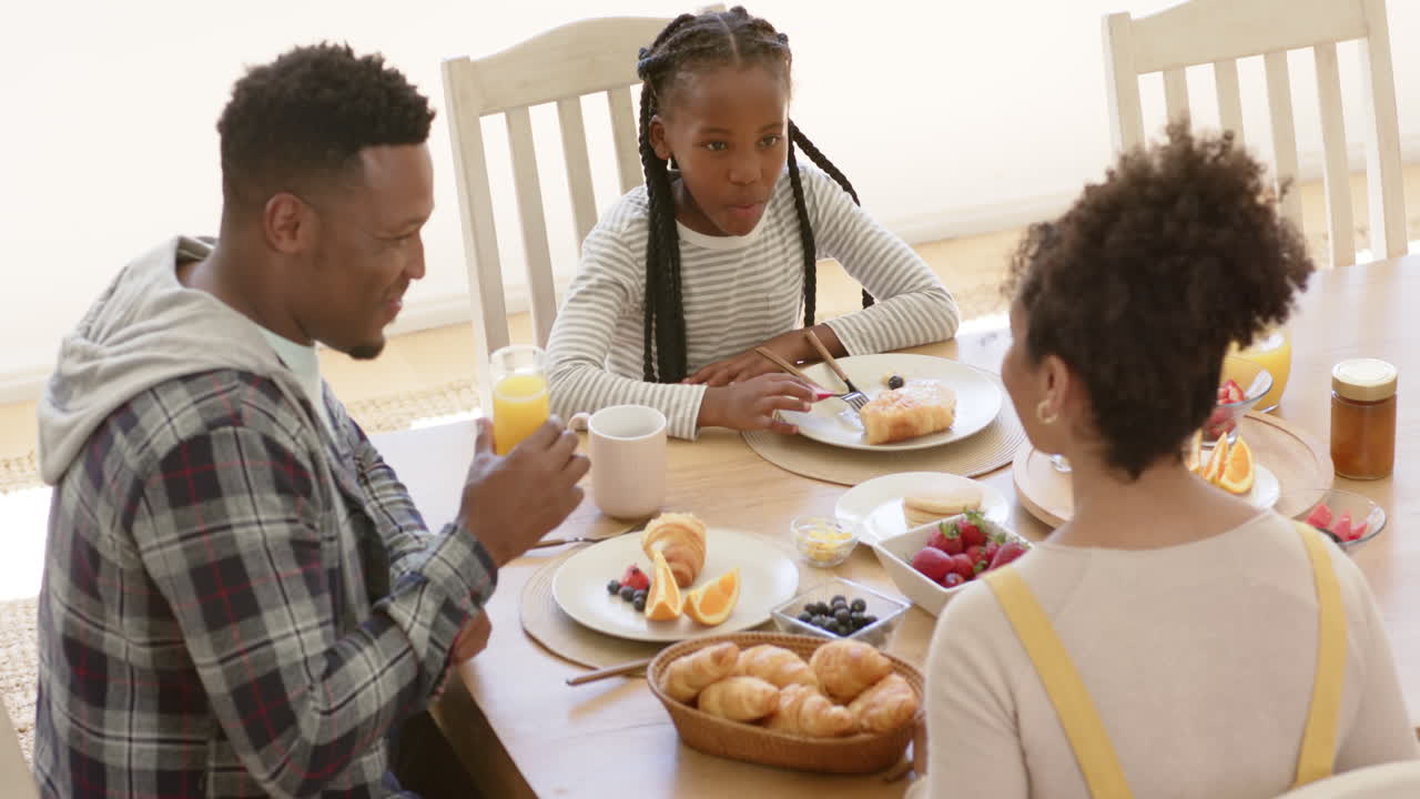 Happy african american parents and daughter having breakfast at home, slow motion