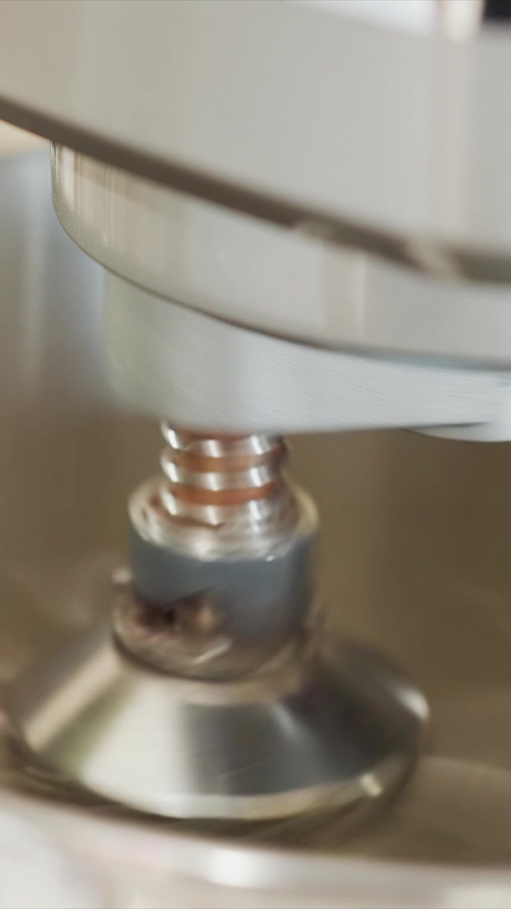 Primo piano di una punta da trapano metallica o di un accessorio per miscelare che gira rapidamente. Superfici lisce e filettature in rame sono. È mostrato un componente di un elettrodomestico da cucina, come parti di un robot da cucina.