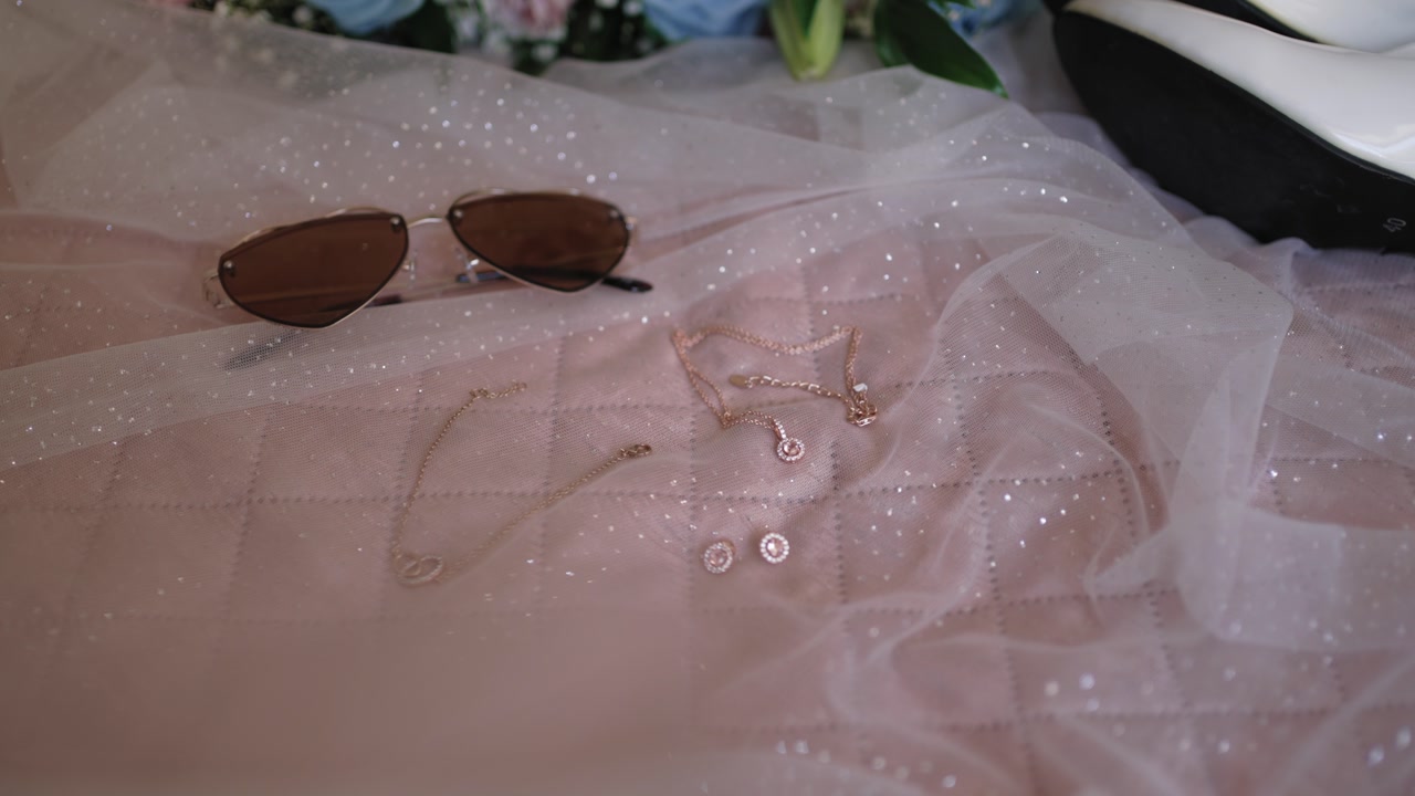 Elegant bridal jewelry and sunglasses placed on soft veil fabric