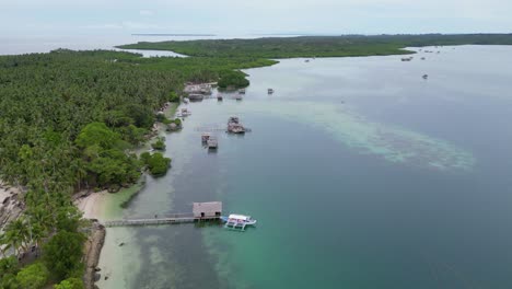 Drone-descends-over-balabac-island-with-palm-trees,-banca-canoe-and-home-on-water
