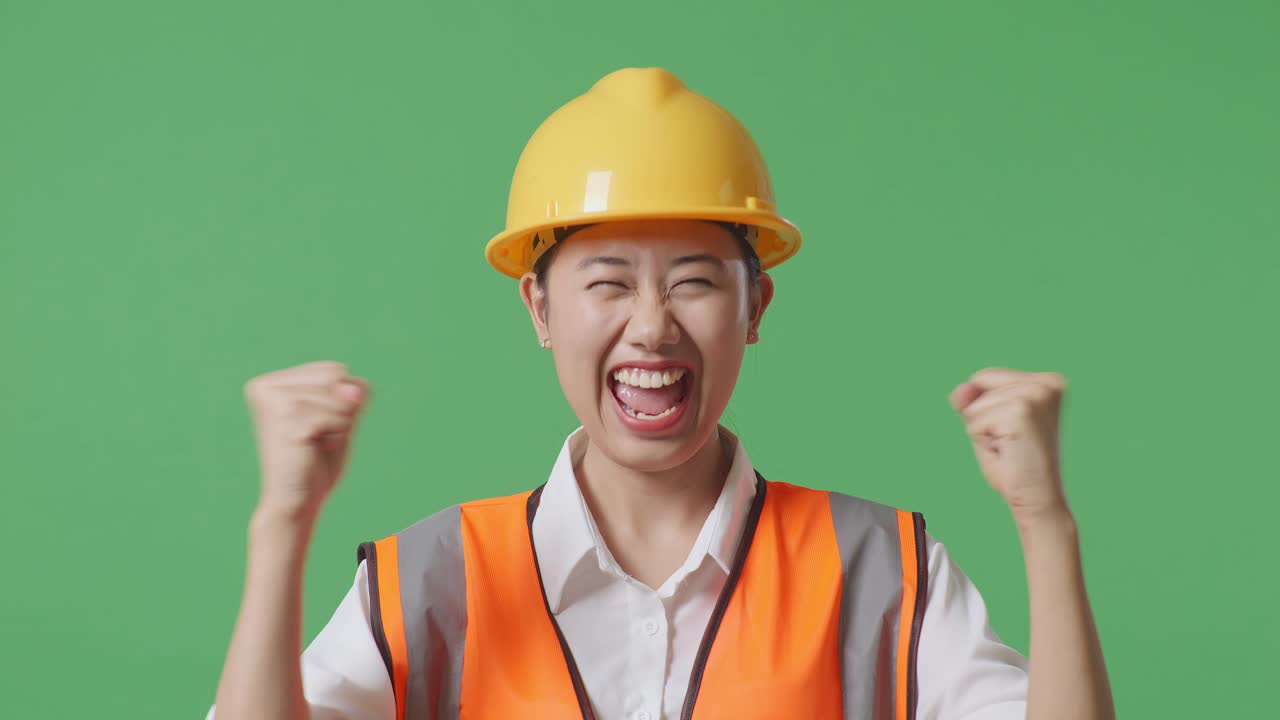 안전 헬을 착용한 아시아 여성 엔지니어가 녹색 스크린을 배경으로 작업하는 것을 축하하는 목표를 외치고 있습니다.