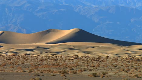 rolling sand dunes under mountain backdrop, death valley, usa. pan left view