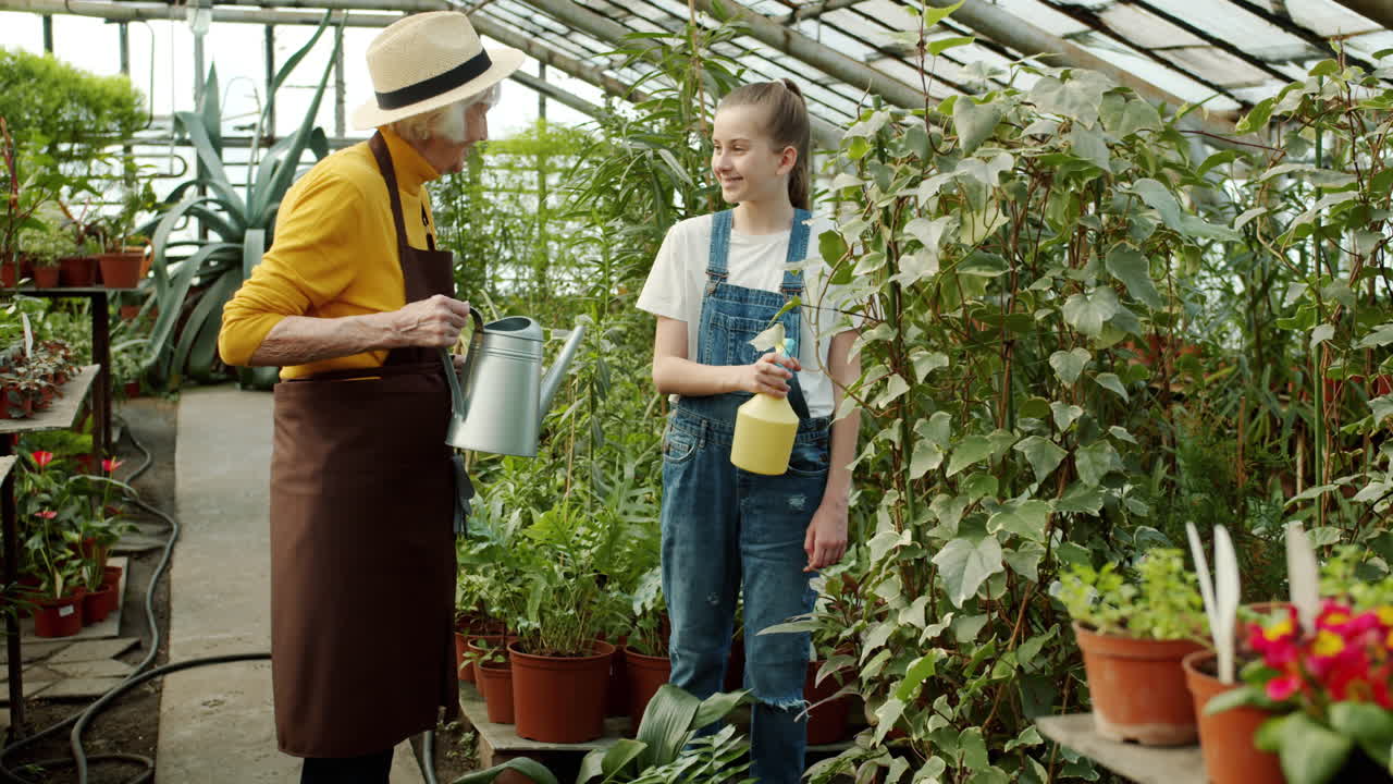 Grandmother and Granddaughter Caring for Plants in a Greenhouse