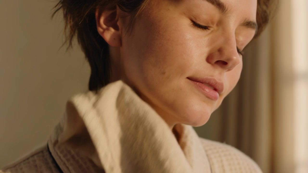 Drying adult woman pressing towel from neck to cheek after washing face in bathroom, with bathrobe