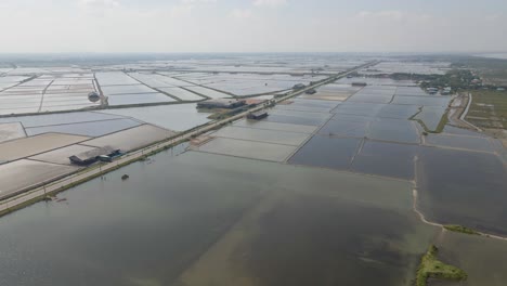 4K-Aerial-Drone-Footage-over-the-Salt-Flats-in-Phetchaburi-Province,-Thailand-with-a-Long-Stretched-Road-to-the-Horizon